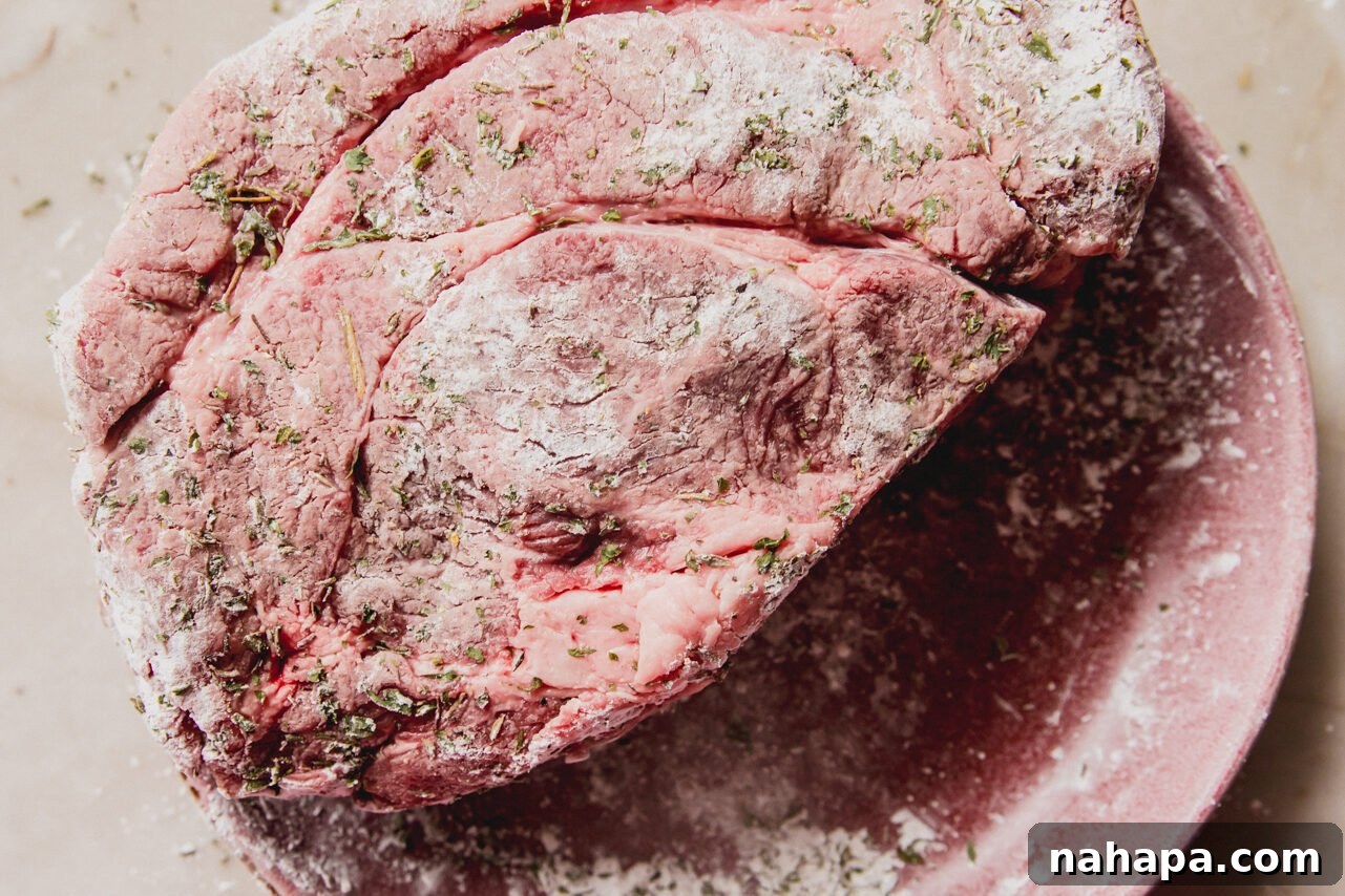 The chuck roast generously coated in a seasoning blend of salt, pepper, herbs, and arrowroot starch, ready for searing.