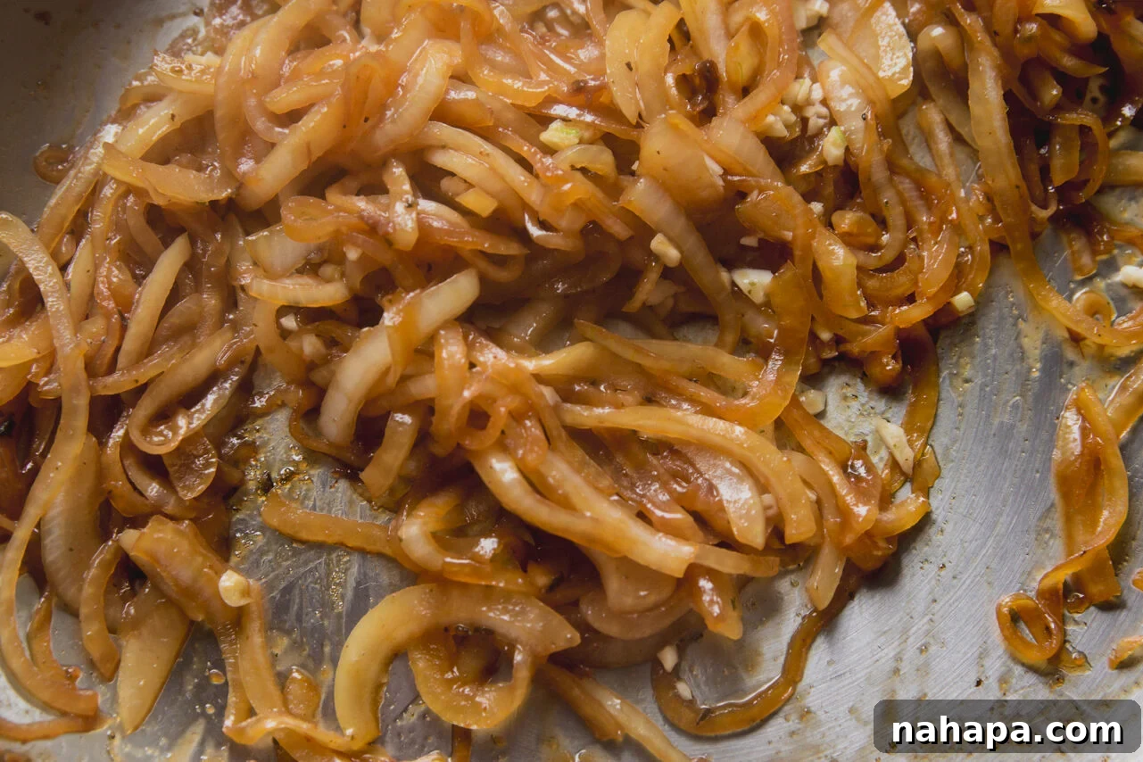 Sliced onions and shallots softening in the pan with coconut aminos, preparing to become caramelized.
