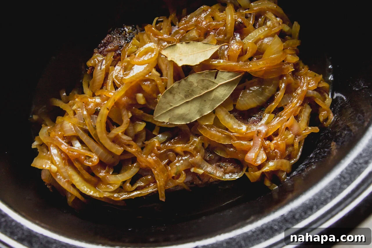 The slow cooker with the chuck roast, topped with the sautéed caramelized onions and bay leaves, ready for slow cooking.