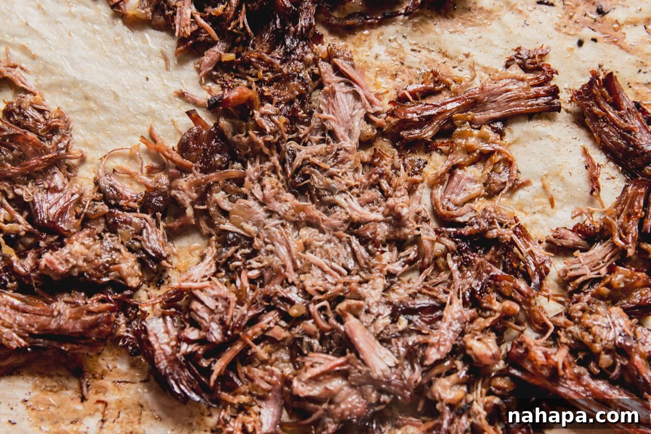 Shredded slow cooker pot roast spread out on a baking sheet lined with parchment paper, crisping in the oven.