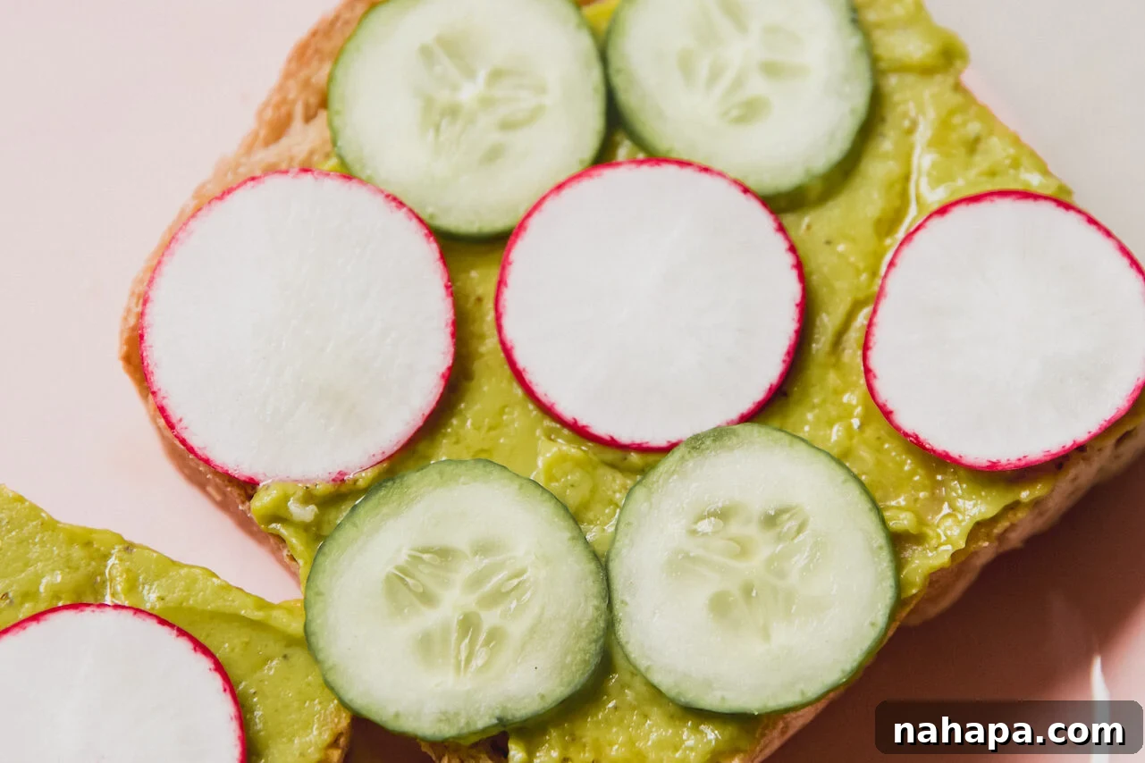 A piece of toasts with avocado, cucumbers, and radish on top.