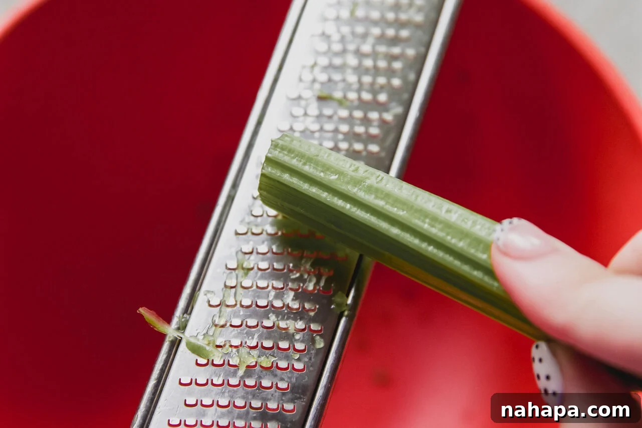 A microplane grater being used to finely shred celery into a bowl with chicken.