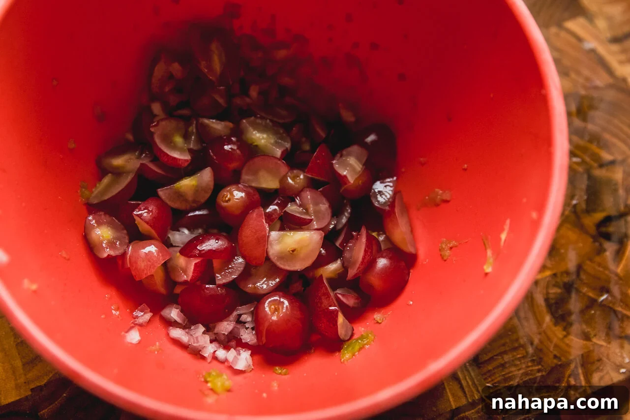 A bowl showing prepped grapes, shallots, and celery mixed with the chicken.