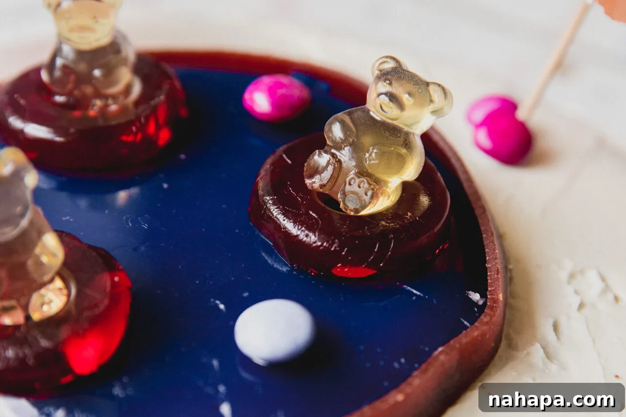 A finished swimming pool cake, exquisitely decorated with a gummy bear lounging in a gummy ring float, surrounded by candy gems and miniature umbrellas.
