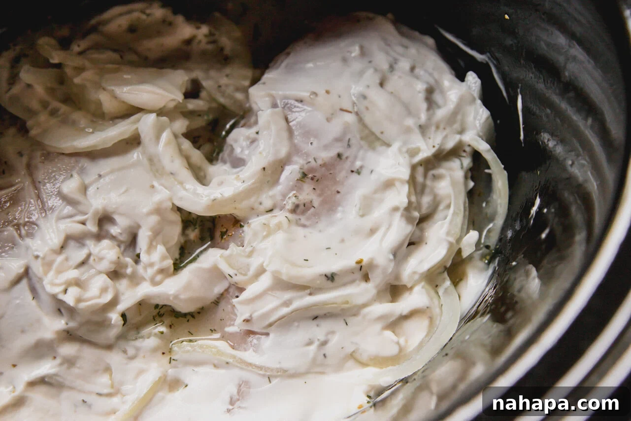 Slow cooker greek chicken uncooked in a slow cooker with sliced onions and yogurt. 
