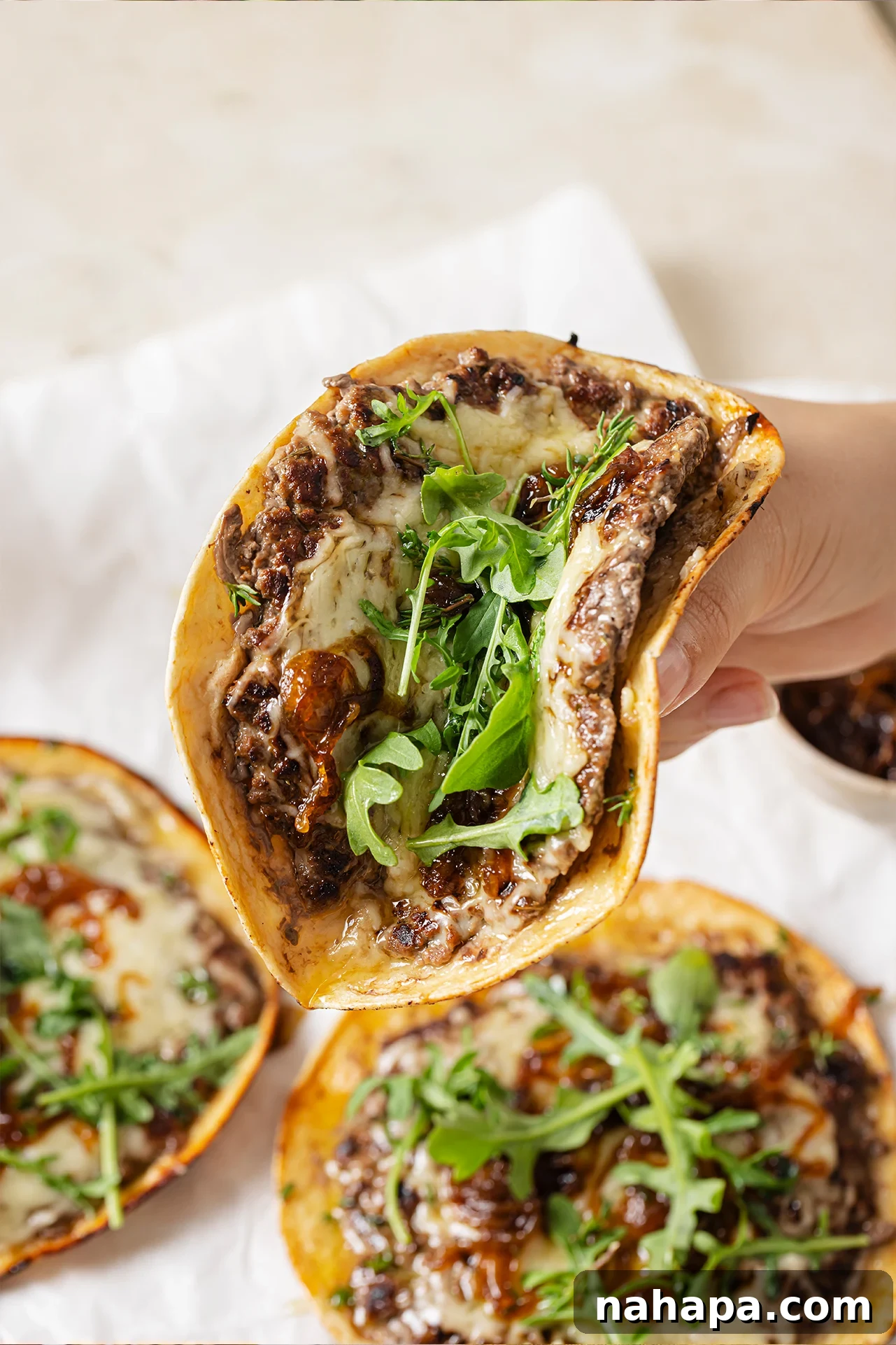 French onion smashburger tacos topped with arugula, with one being picked up, partially folded.