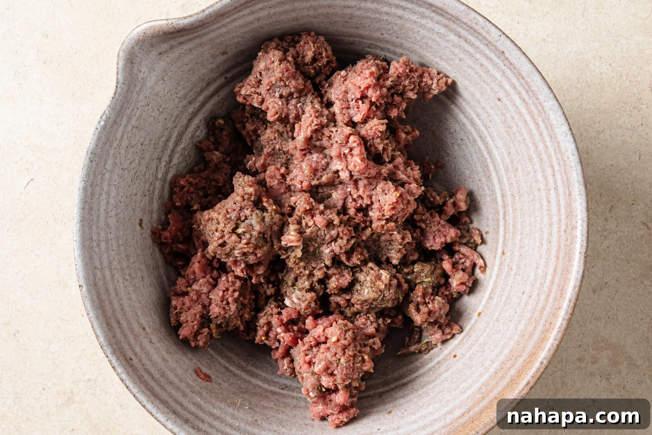 Ground beef being mixed with an array of spices and coconut aminos in a bowl.