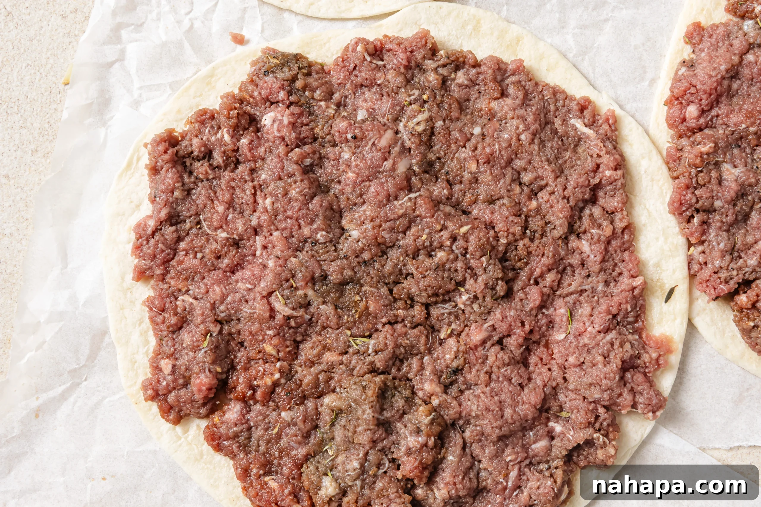 A raw ground beef patty being spread thinly onto an almond flour tortilla with a fork.