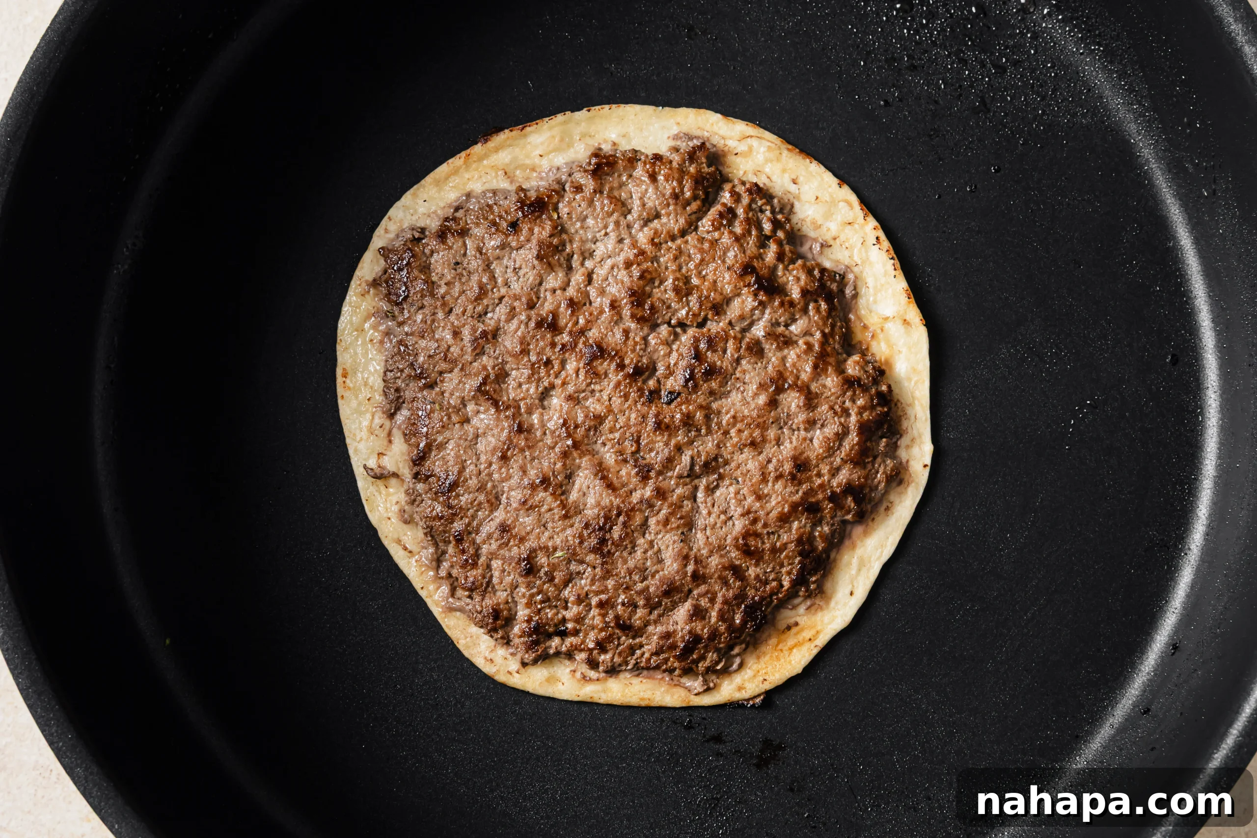 One French onion smashburger taco cooking meat-side down in a hot pan, crisping up.