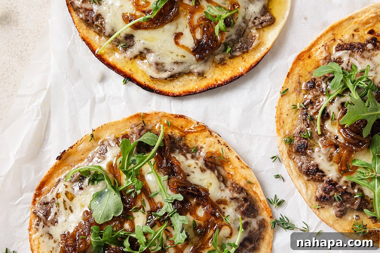 Three cooked smashburger tacos topped with melted cheese and caramelized onions, ready for final garnishes.