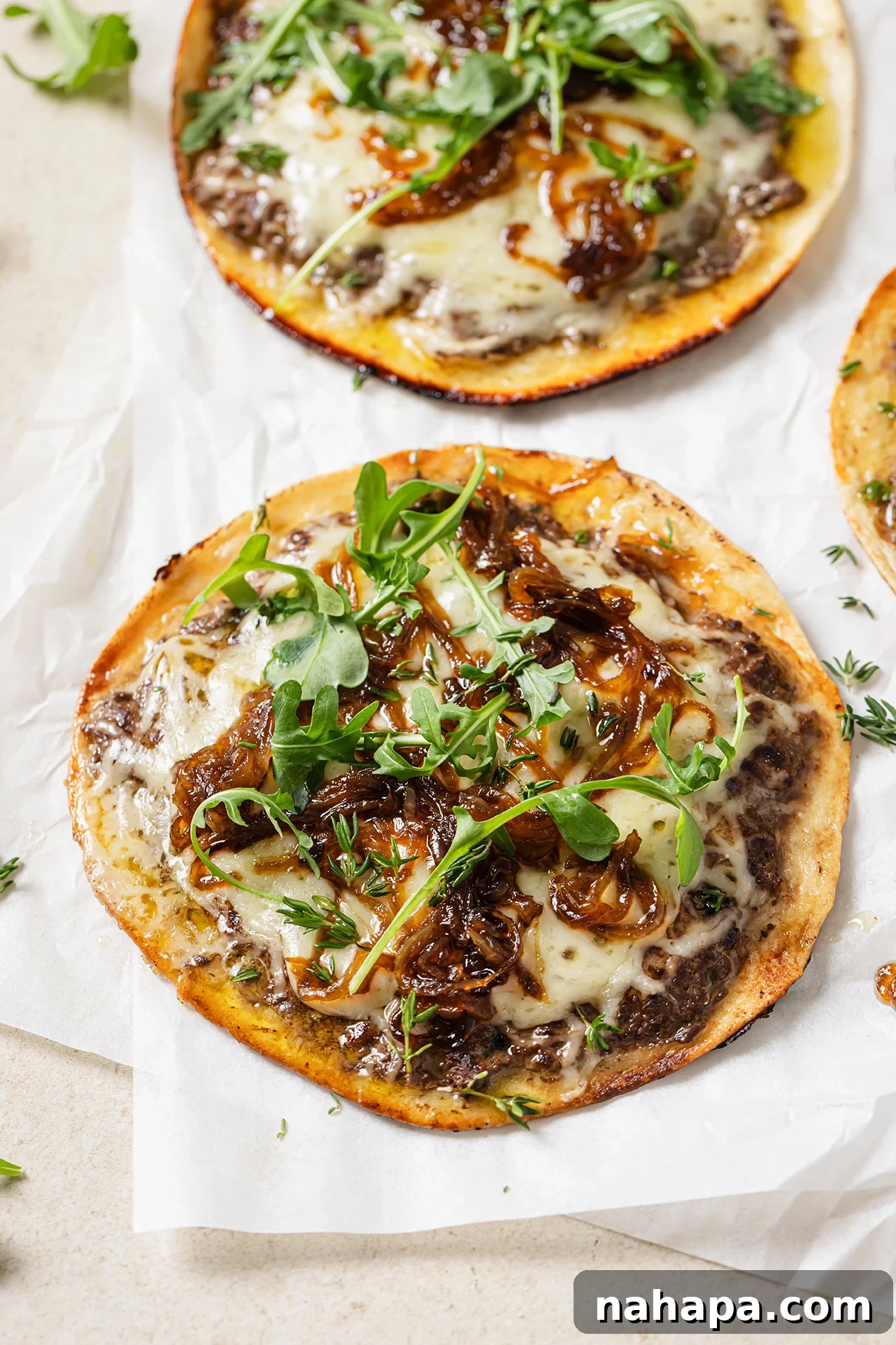 A vibrant close-up of French onion smashburger tacos, generously topped with arugula and fresh thyme.