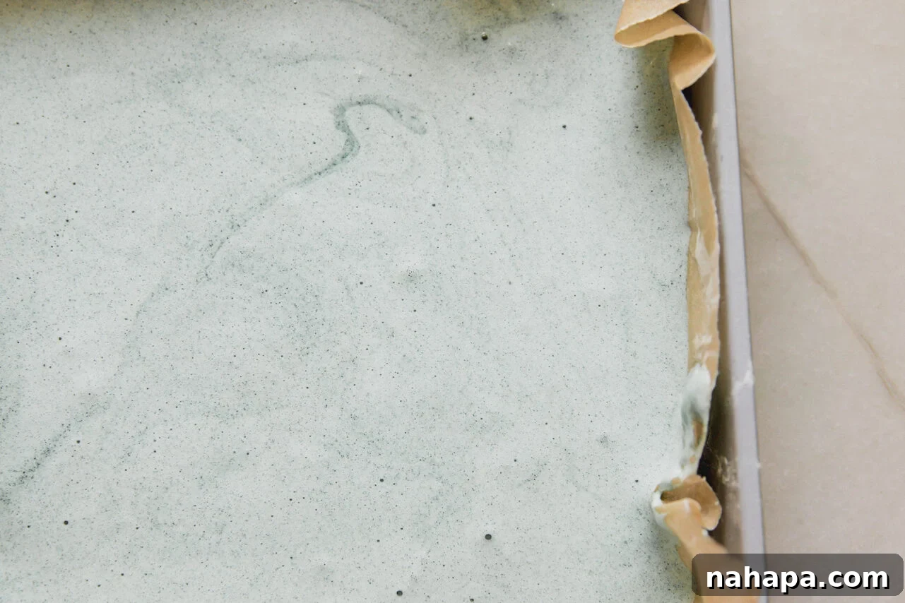 Watermelon Cloud Treats 5 The vibrant green marshmallow mixture evenly spread in a parchment-lined baking pan, ready to set.
