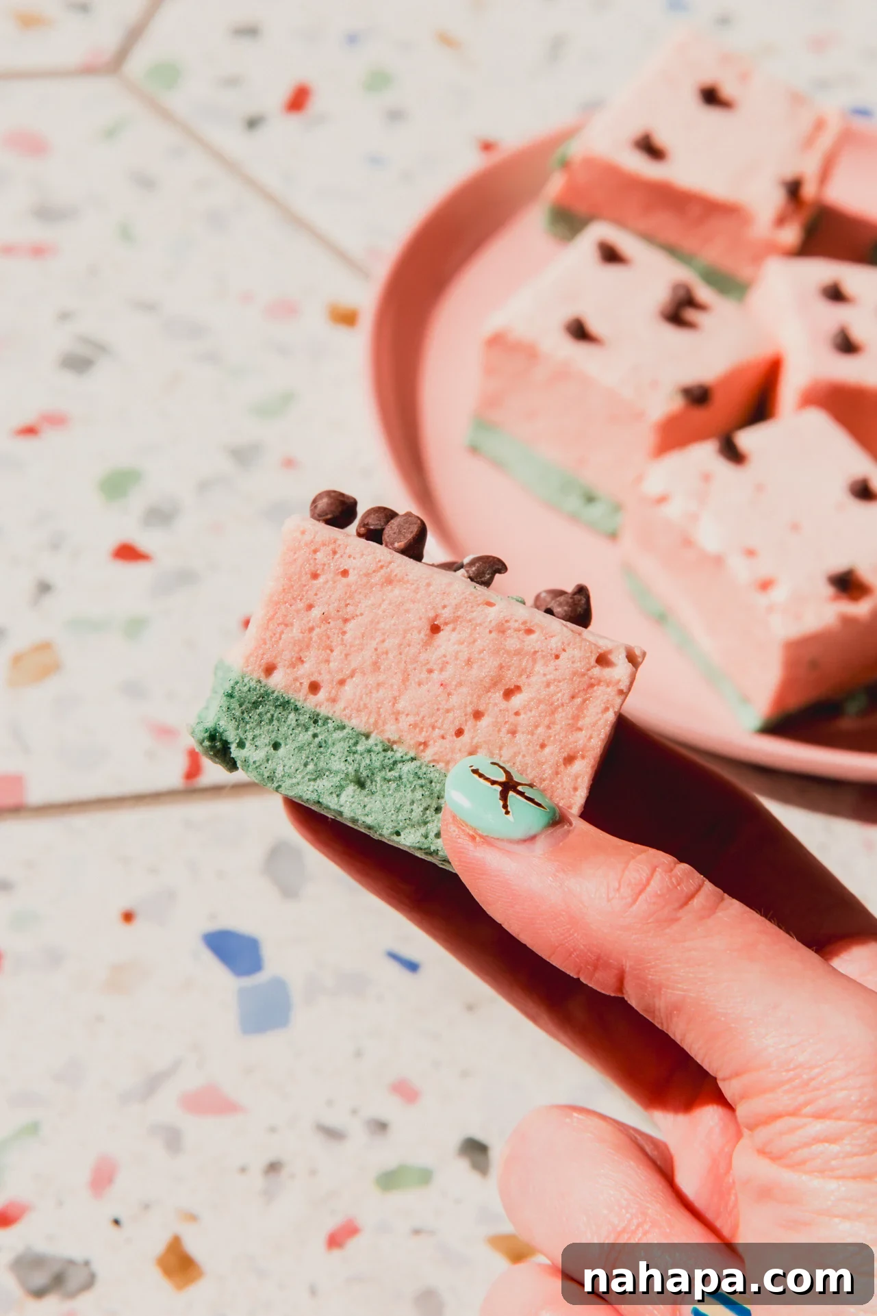 Watermelon Cloud Treats 10 A hand reaching for one homemade watermelon marshmallow, ready to be enjoyed as a sweet treat.