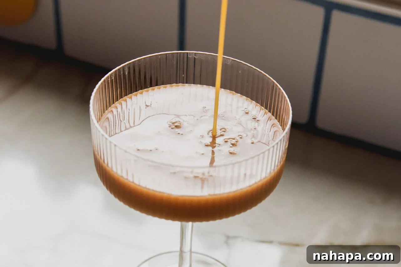 Espresso Velvet Zero 5 Espresso martini mocktail being poured from a shaker into an elegant cocktail glass, showing its rich color and foamy texture.