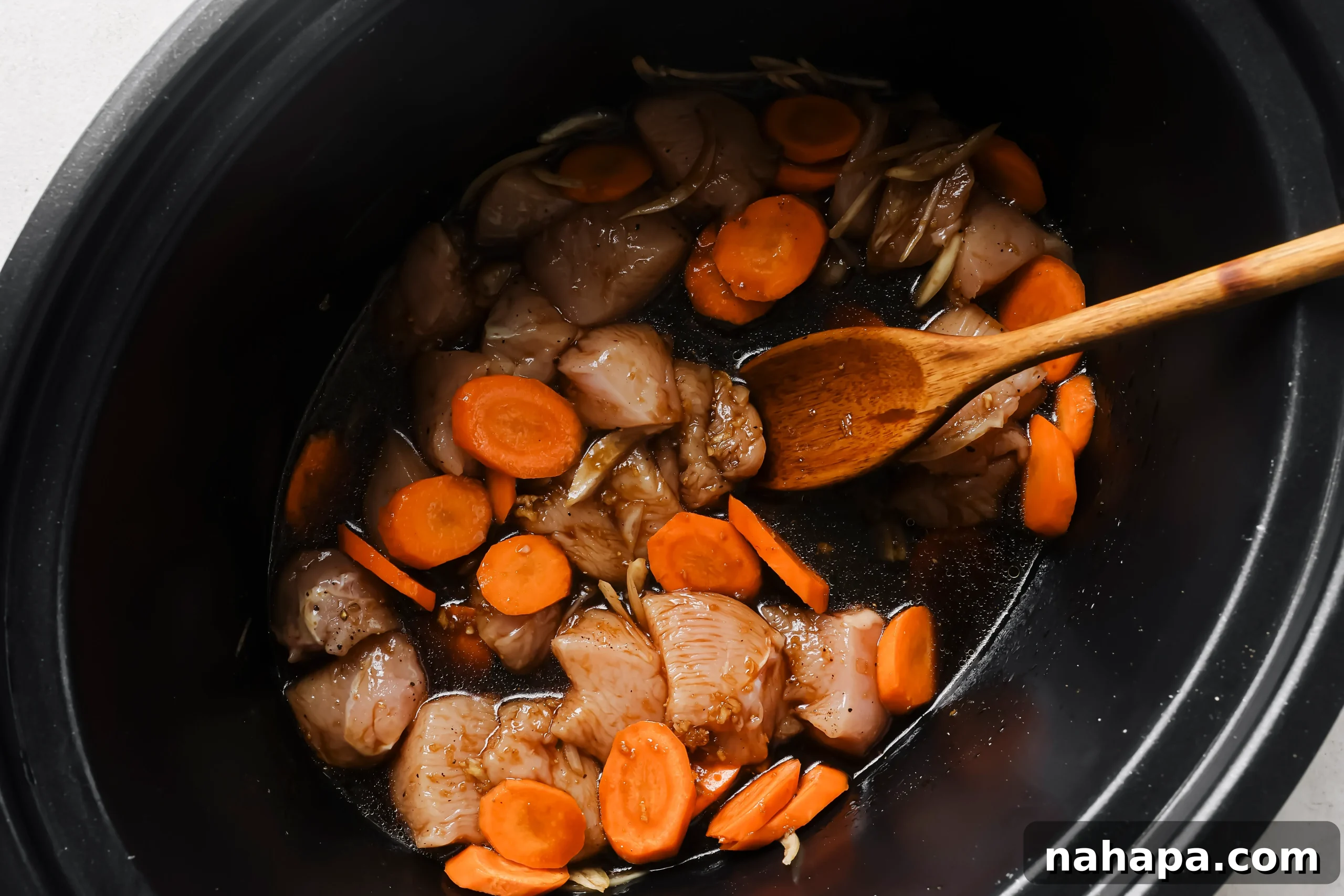 Cubed chicken and diagonally cut carrots in a slow cooker, with the whisked sauce being poured over them.