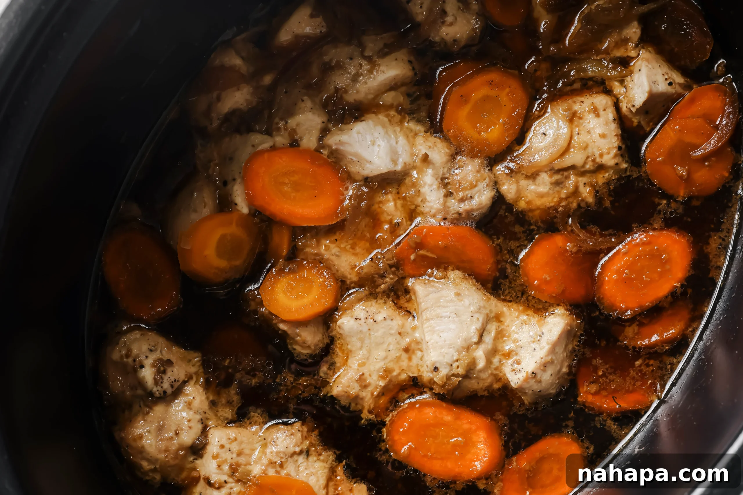 Chicken and carrots cooking in the slow cooker, submerged in the sauce.