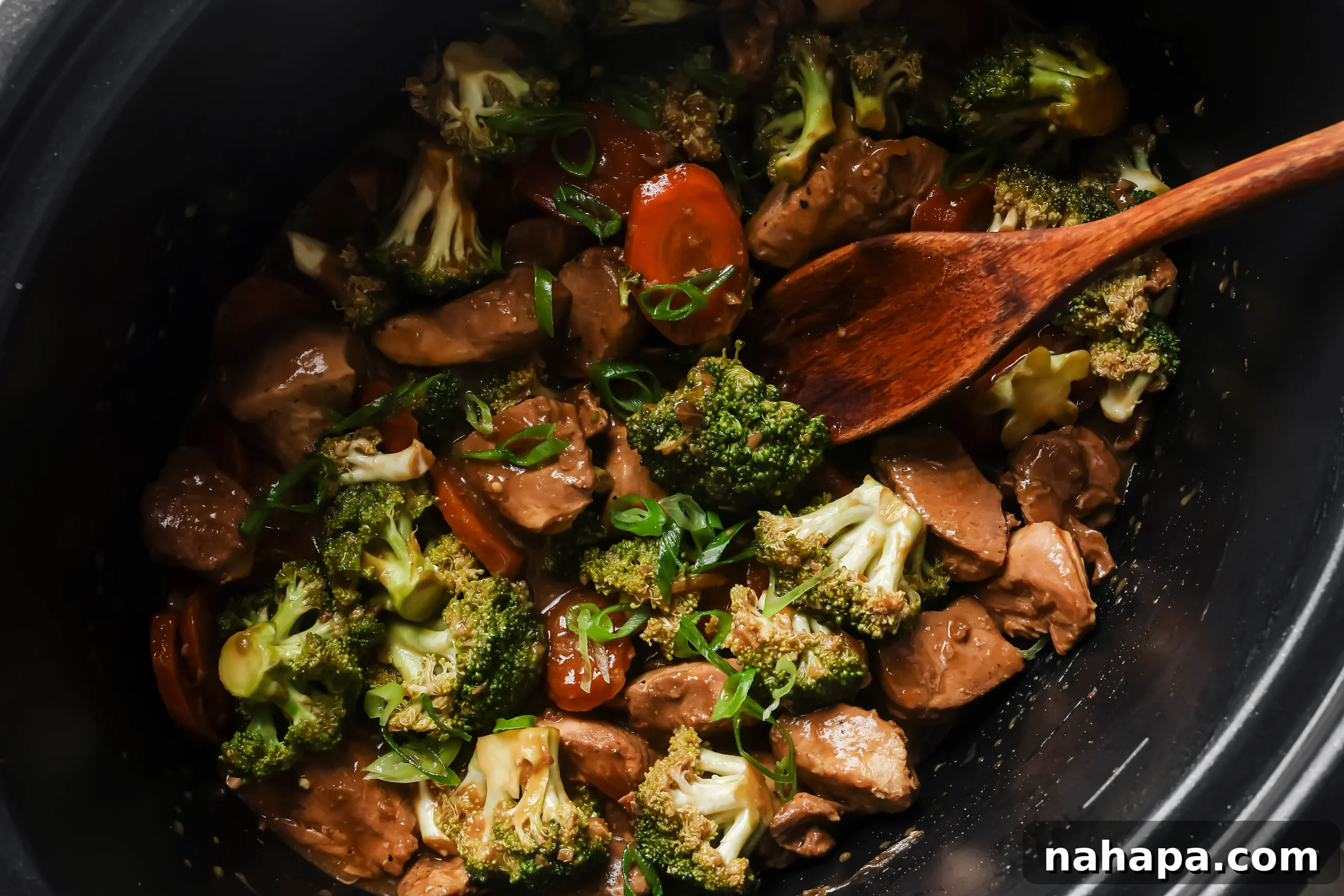 Fully cooked chicken and broccoli in a slow cooker, with thickened sauce and green onions being added.