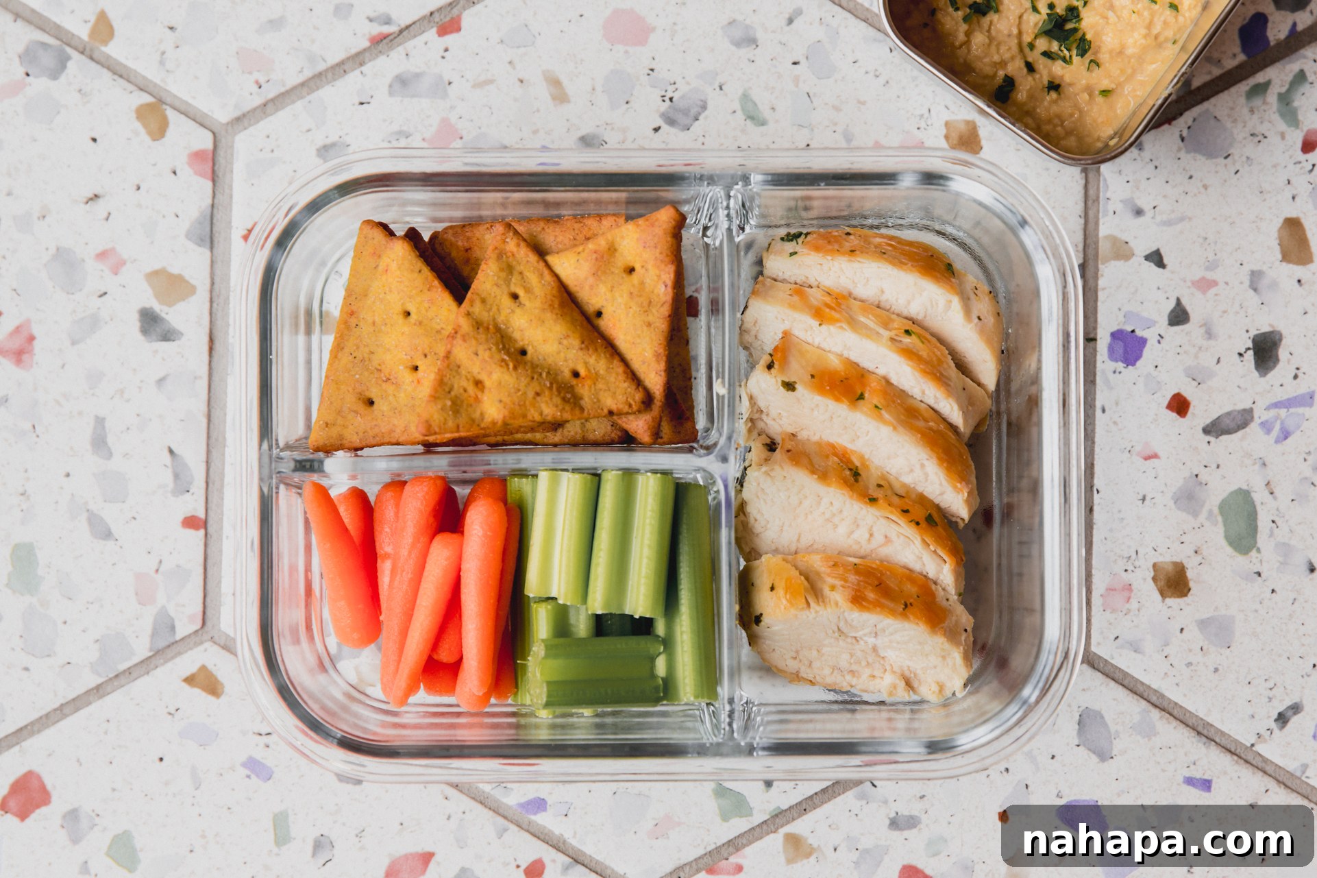 Clear divided lunch container with chicken, veggies, and pita chips.