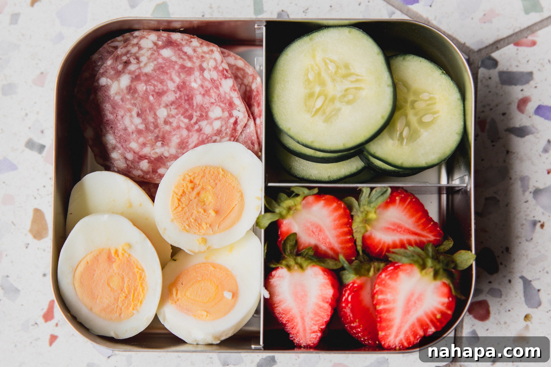 Divided lunch container with lunch meat, sliced boiled eggs, sliced cucumber, and sliced strawberries. 