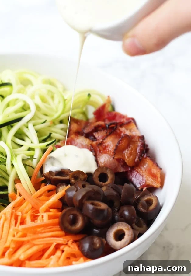 Paleo AIP Whole30 Bacon Ranch Zucchini Noodle Pasta Salad 5 A bowl filled with zoodles, carrots, bacon, and olives in it, dressed with ranch