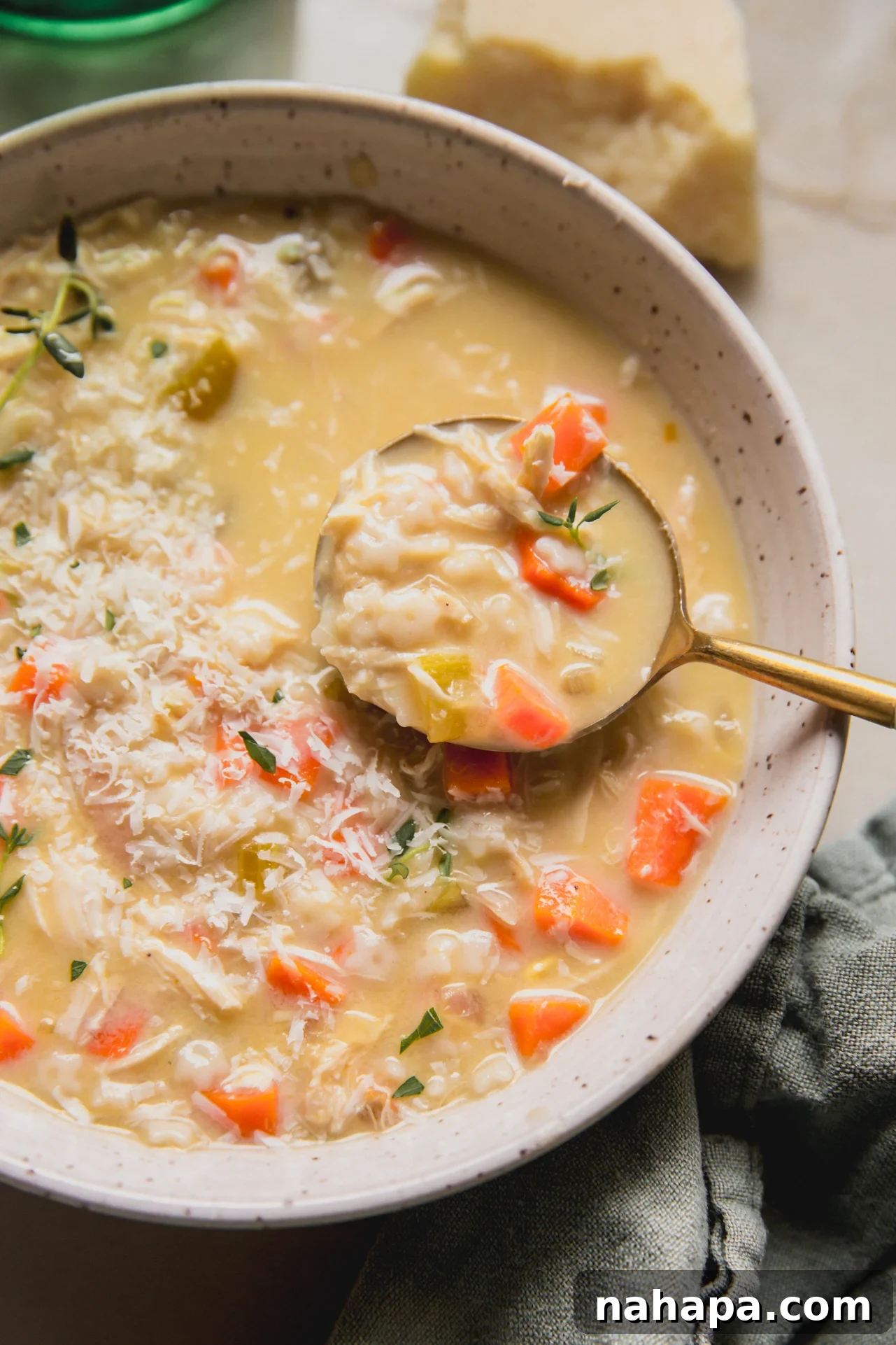 Comforting gluten-free pastina chicken soup in a bowl, garnished with fresh thyme and grated cheese, with a spoon ready to serve.