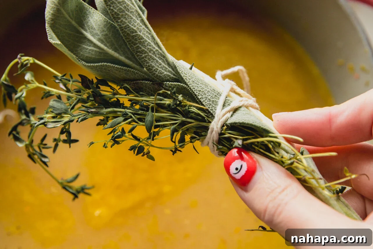 A hand adding a bundle of fresh herbs and a Parmesan rind to a pot of simmering soup.