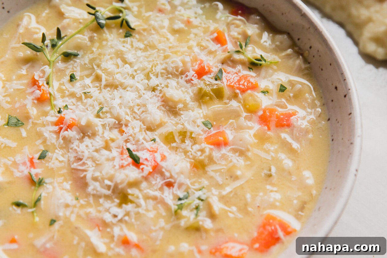 A serving of gluten-free chicken pastina soup, beautifully garnished with fresh thyme and grated Parmesan cheese.