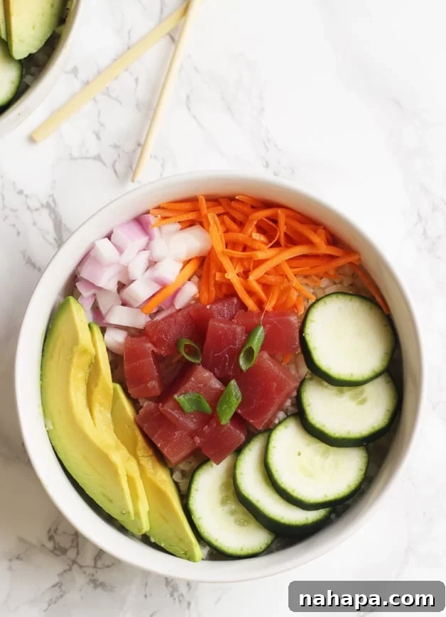 Effortless Whole30 Paleo AIP Poke Bowl 3 A close-up shot of a fresh poké bowl featuring glistening tuna chunks, sliced avocado, crunchy cucumbers, and a sprinkle of green onions, ready to be enjoyed.