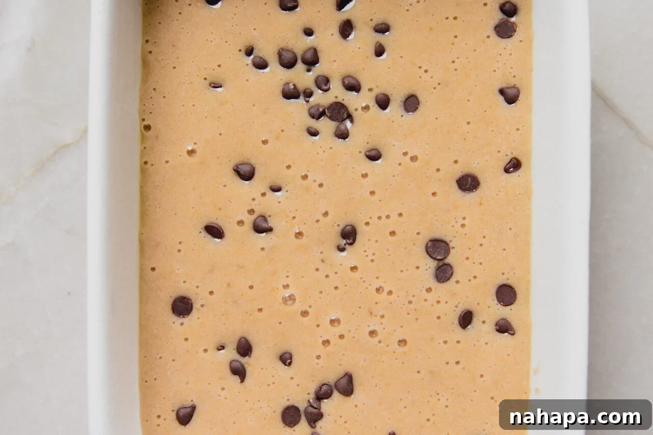 Banana protein breakfast cake batter poured into a baking dish and topped with mini chocolate chips.