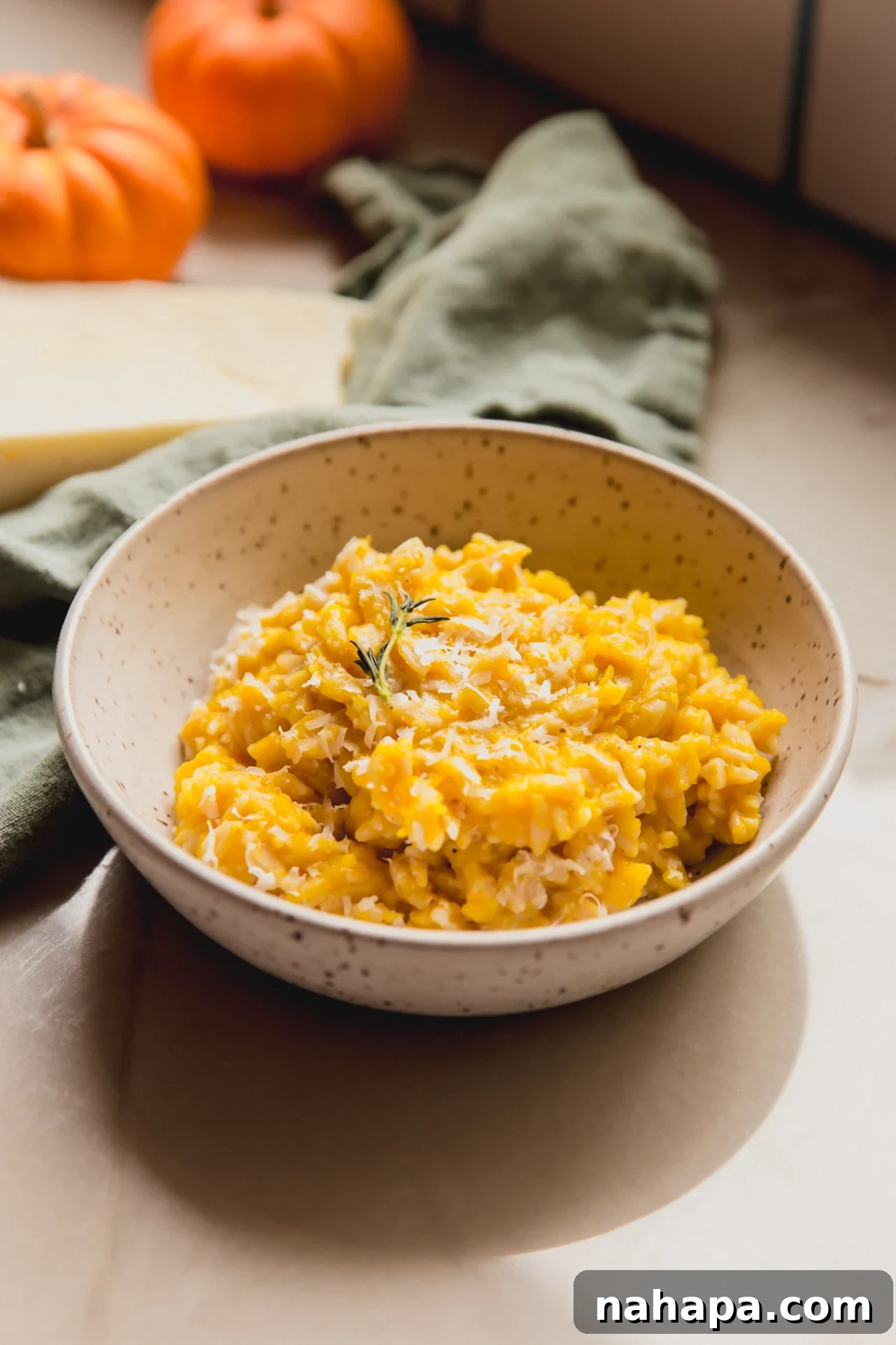 A bowl of creamy pumpkin orzo pasta, garnished generously with fresh thyme leaves, against a warm, inviting background, ready to be served.