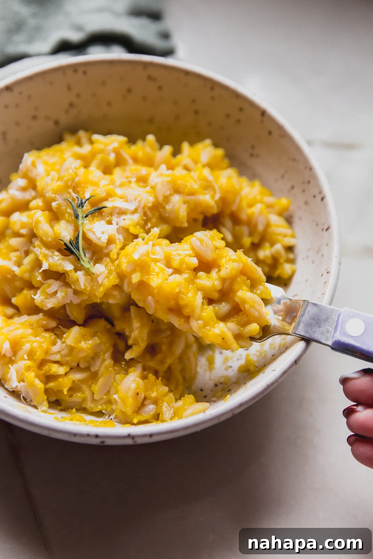 A spoonful of creamy pumpkin orzo being lifted from a rustic bowl, showcasing its rich texture and flecks of herbs, ready to be enjoyed.