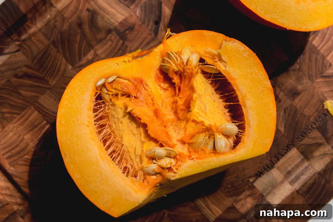 A small sugar pumpkin with the stem removed, perfectly sliced in half, revealing its vibrant orange flesh and seeds.