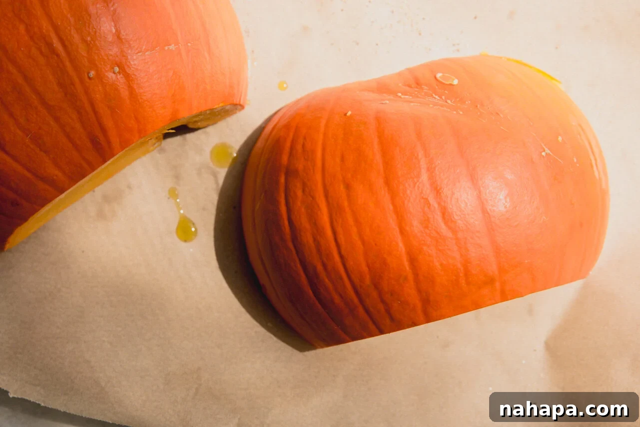 Two halves of a sugar pumpkin placed cut-side down on a parchment-lined baking sheet, ready for roasting.