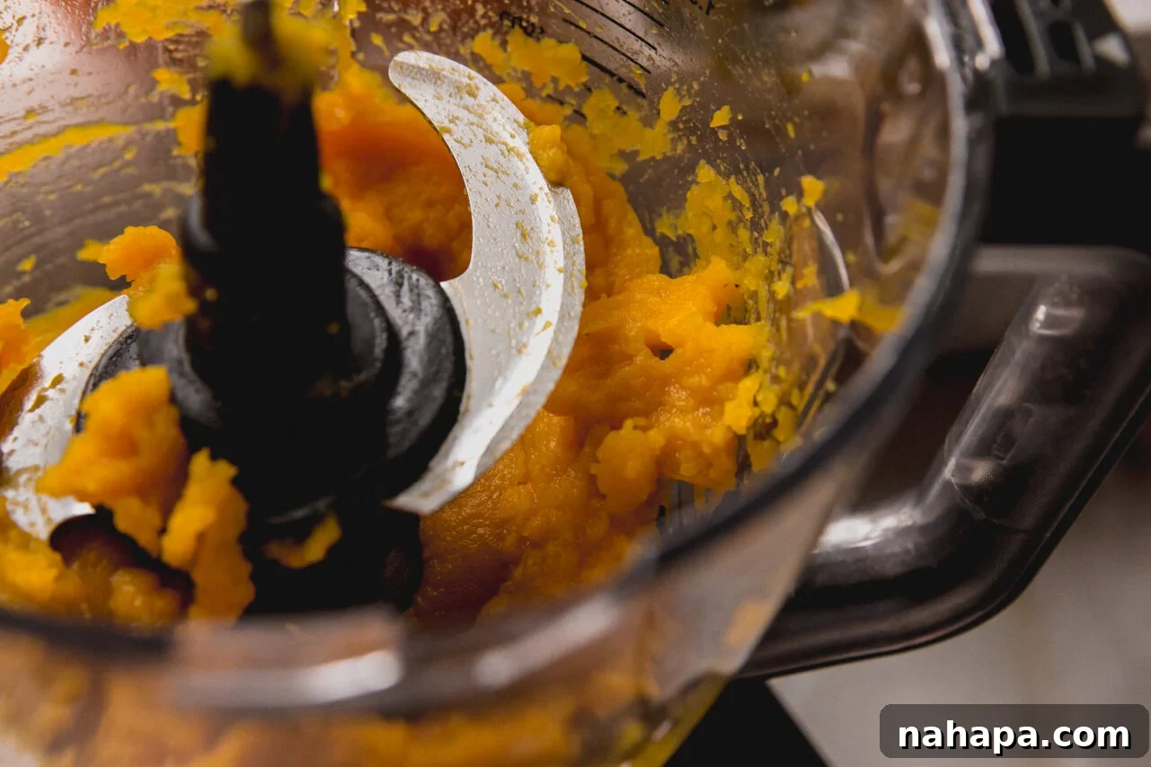 The soft, roasted pumpkin flesh being scooped into a food processor to be blended into a smooth puree.