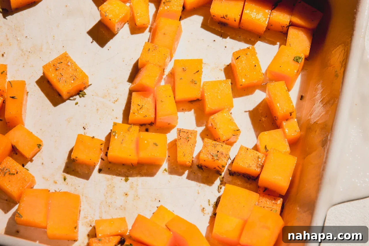Diced butternut squash seasoned with avocado oil and herbs in a casserole dish.
