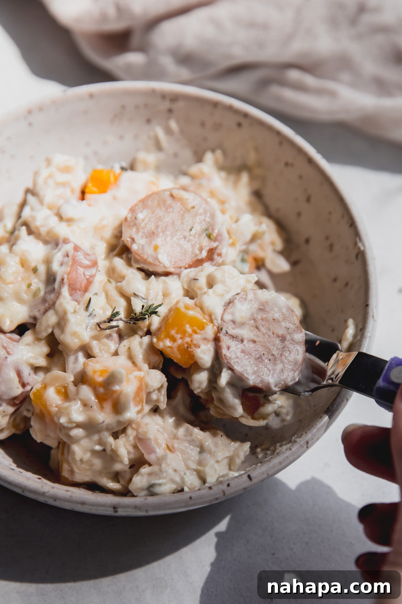 A bowl of creamy chicken sausage and orzo with a spoon taking a bite.