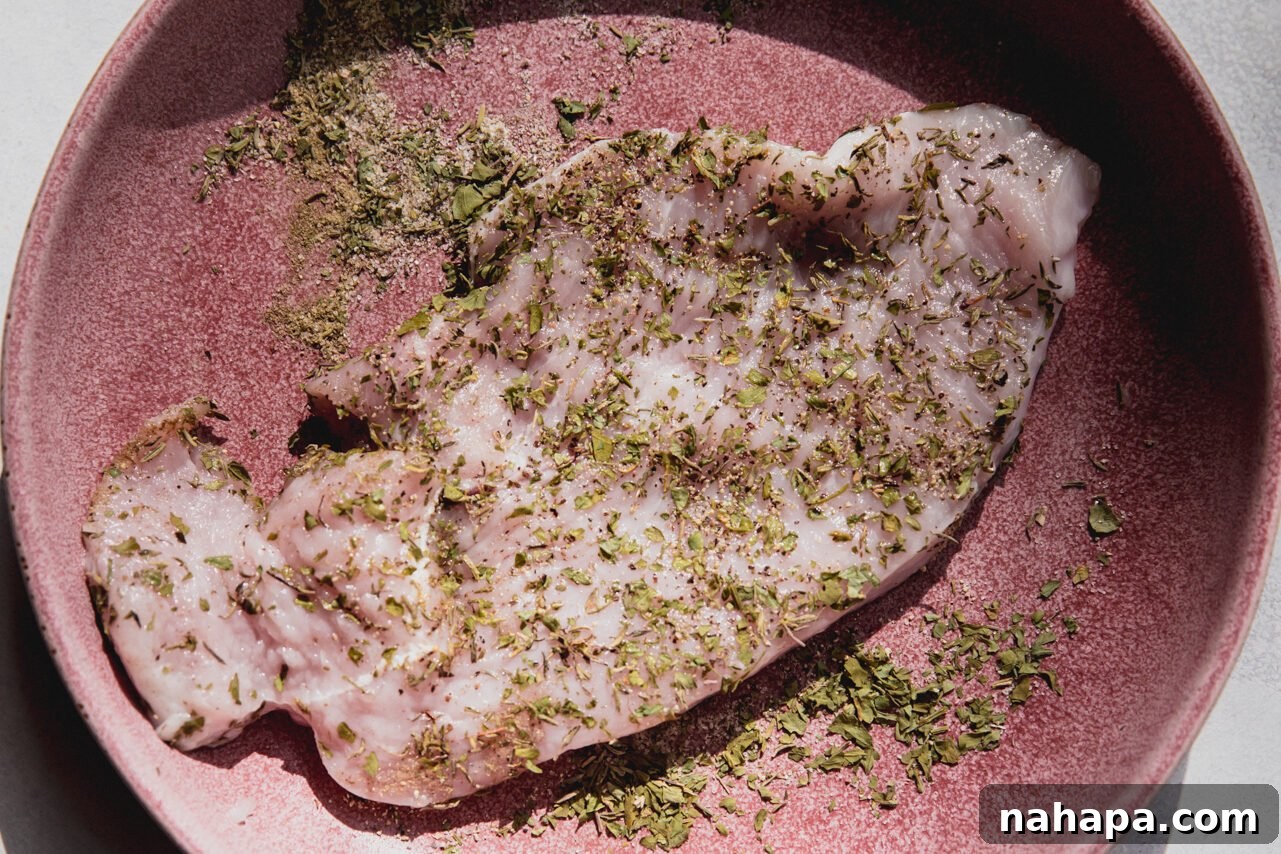 Raw turkey cutlet generously coated with a blend of aromatic herbs and spices, ready for cooking.