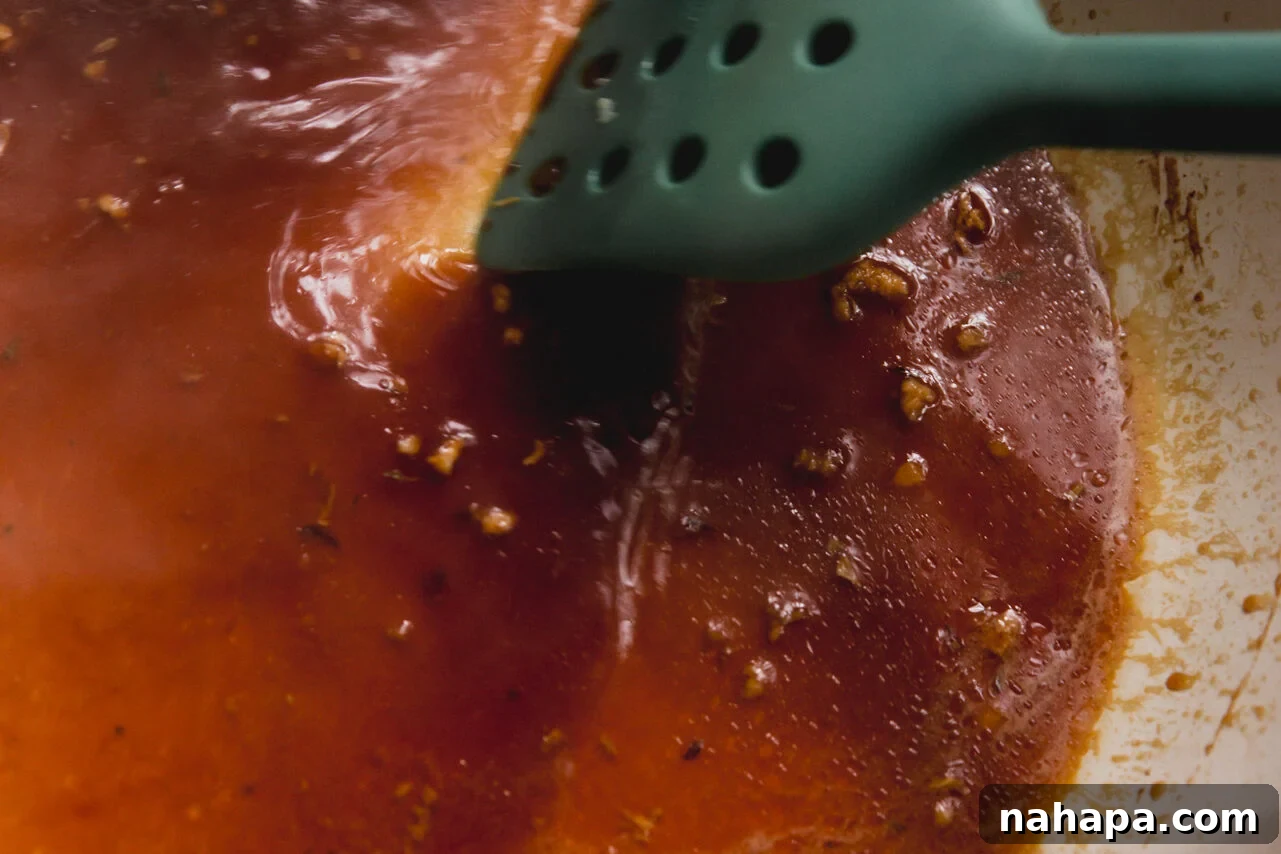 A cooking pan being deglazed with coconut aminos, capturing the flavorful browned bits from the turkey.