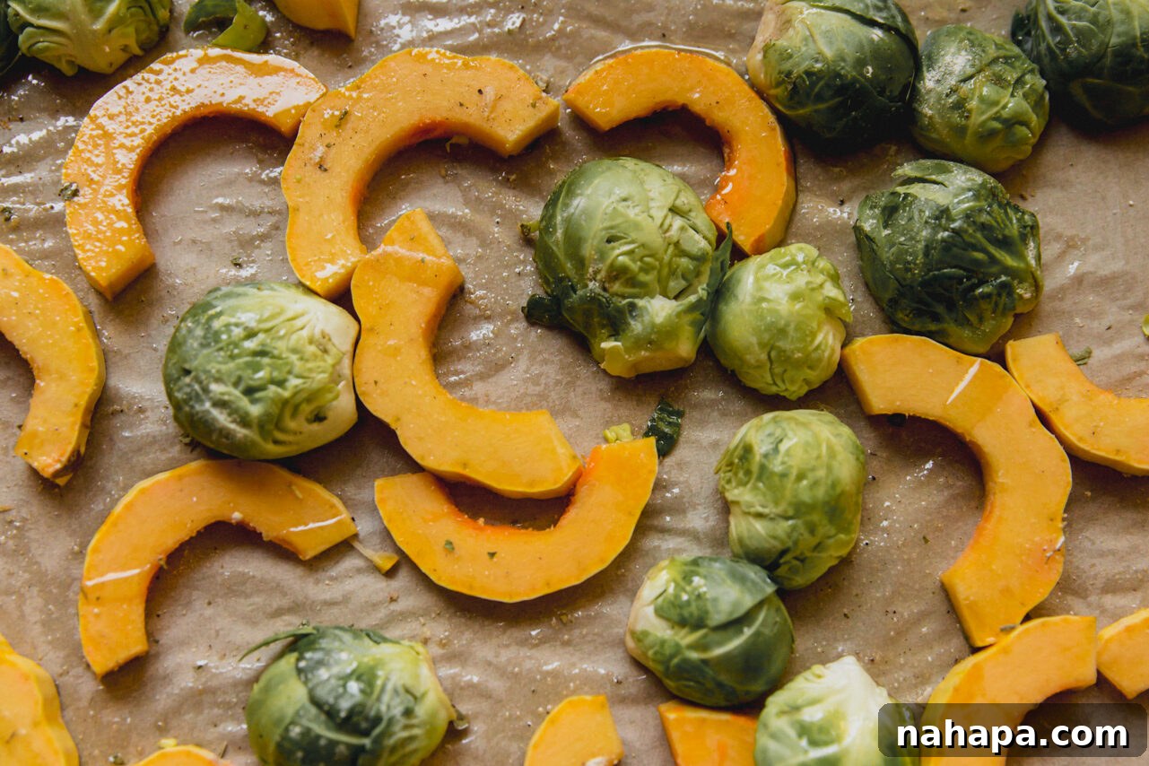 Golden Harvest Chicken & Squash Bowl 4 Delicata squash half-moons and halved Brussels sprouts seasoned with herbs and avocado oil on a baking sheet, ready for roasting.
