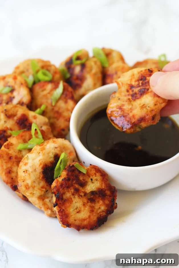 Crispy golden brown Asian Chicken Poppers arranged on a plate with a side of dipping sauce, garnished with fresh green onions.