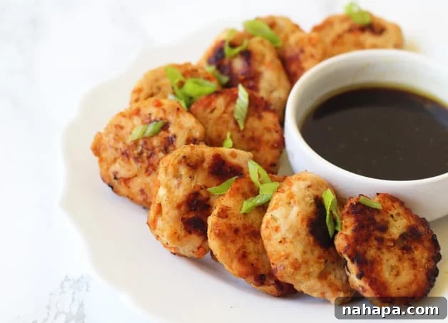 A close-up of several baked Asian Chicken Poppers, golden brown and garnished with fresh green onion, ready to be served.