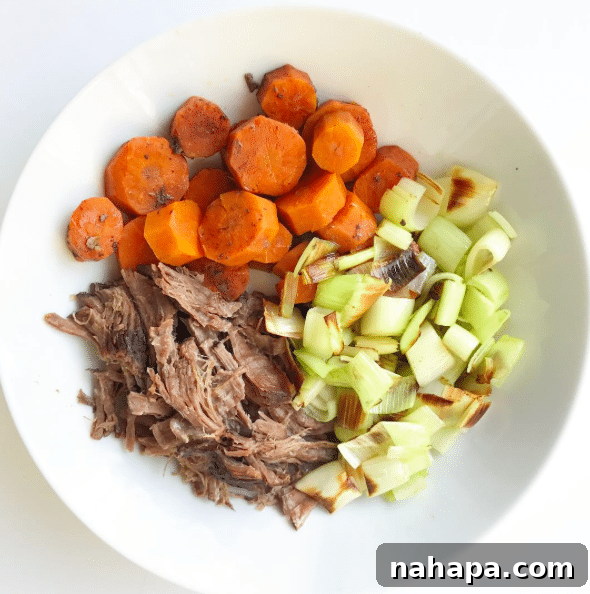 A bowl with shredded beef, roasted carrots, and celery in it.