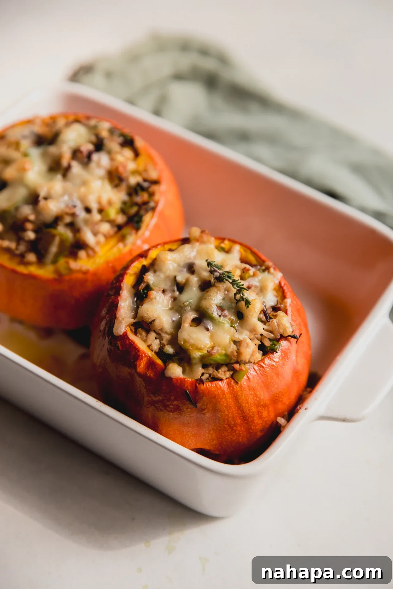 Two roasted stuffed pumpkins in a baking dish, garnished with fresh herbs.