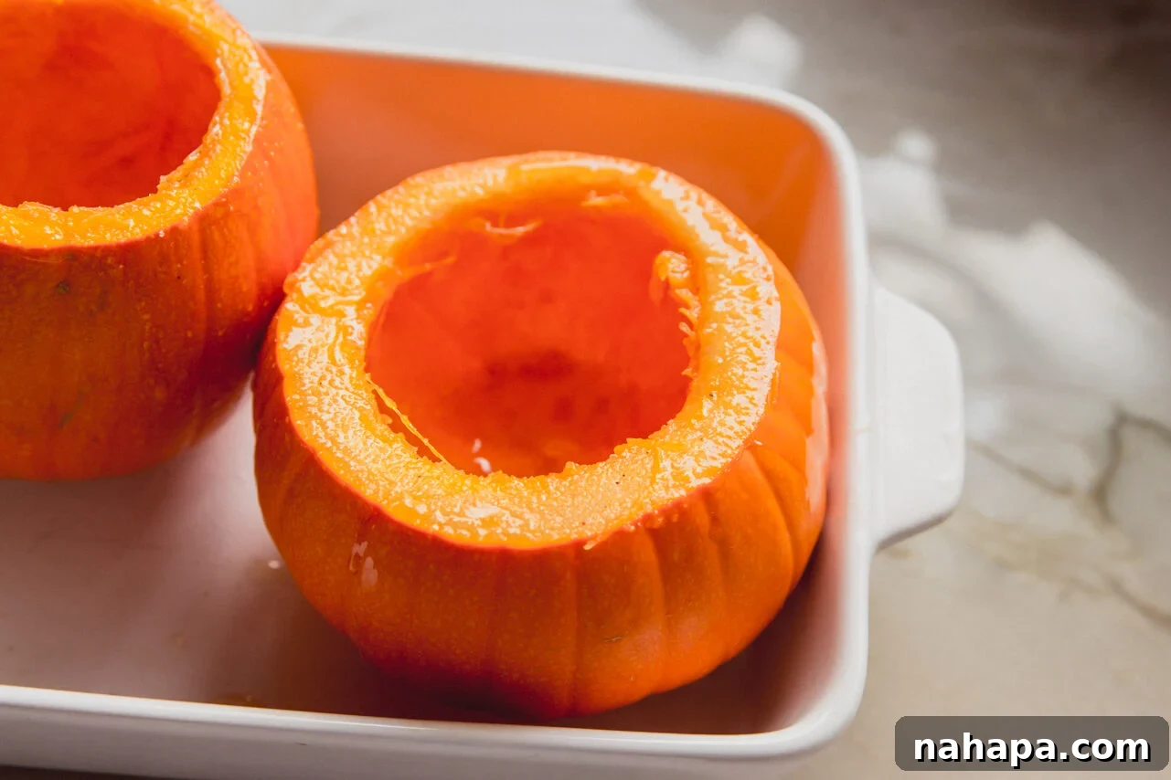 Uncooked pumpkins with their tops cut off and insides scooped out, arranged in a baking dish.