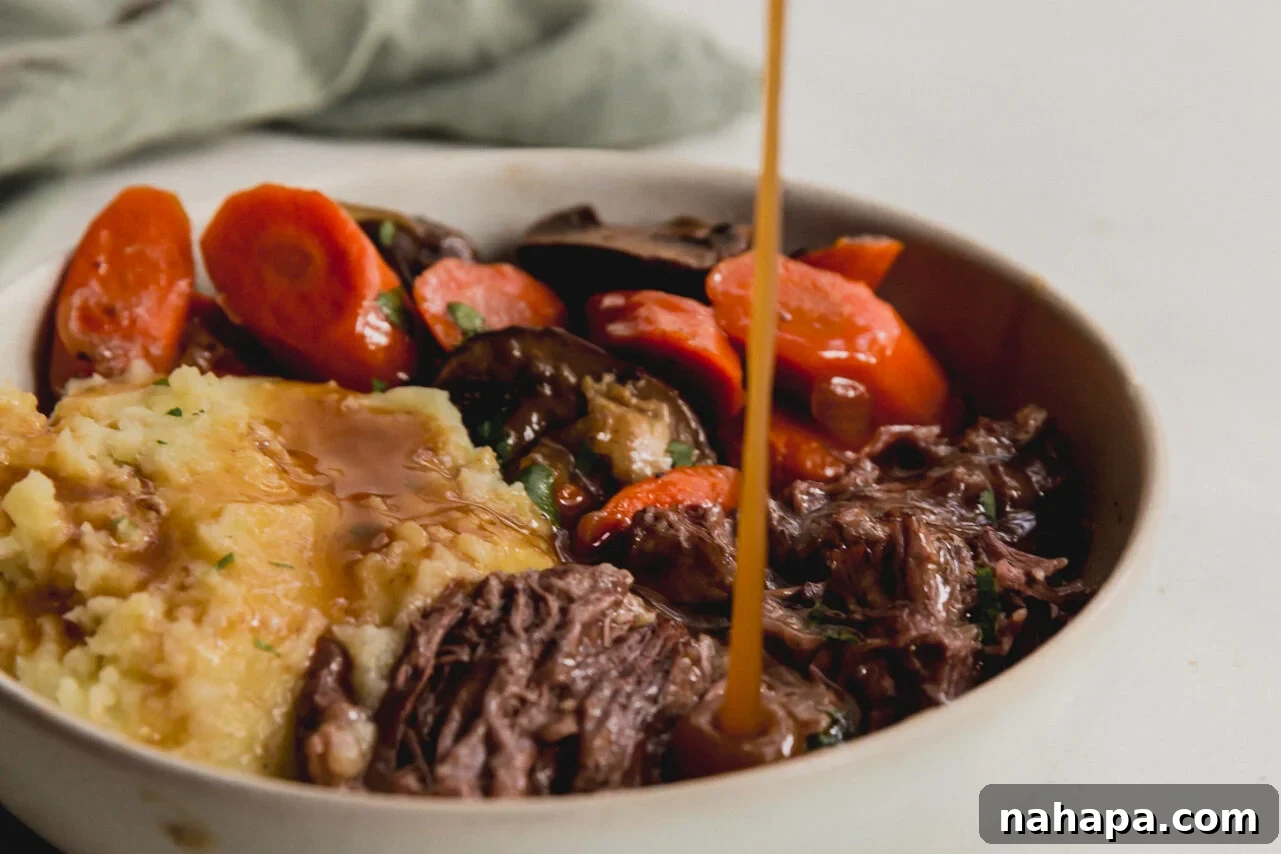 A bowl of pot roast, sweet potatoes, and vegetables, with gravy being poured generously over top.
