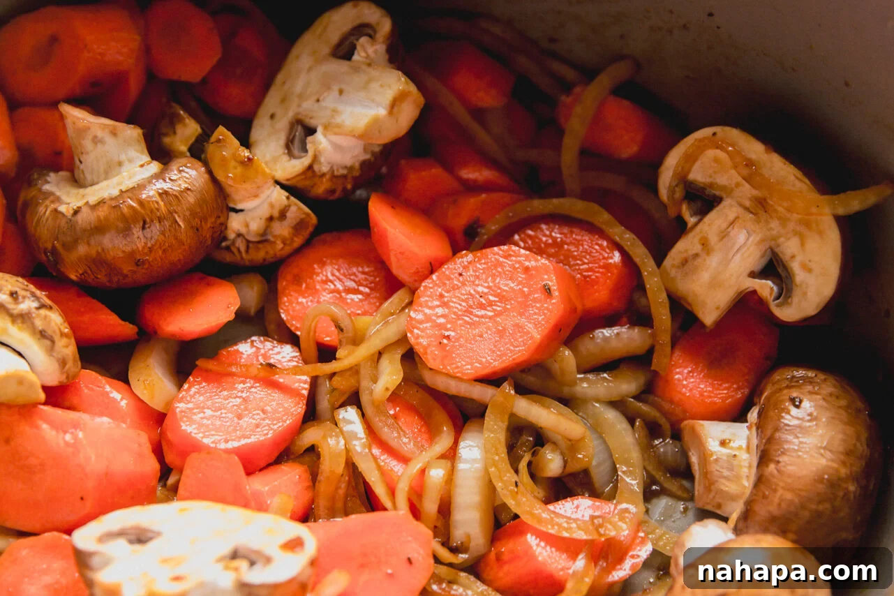 Sliced onions, garlic, mushrooms, and carrots sautéing in a Dutch oven.