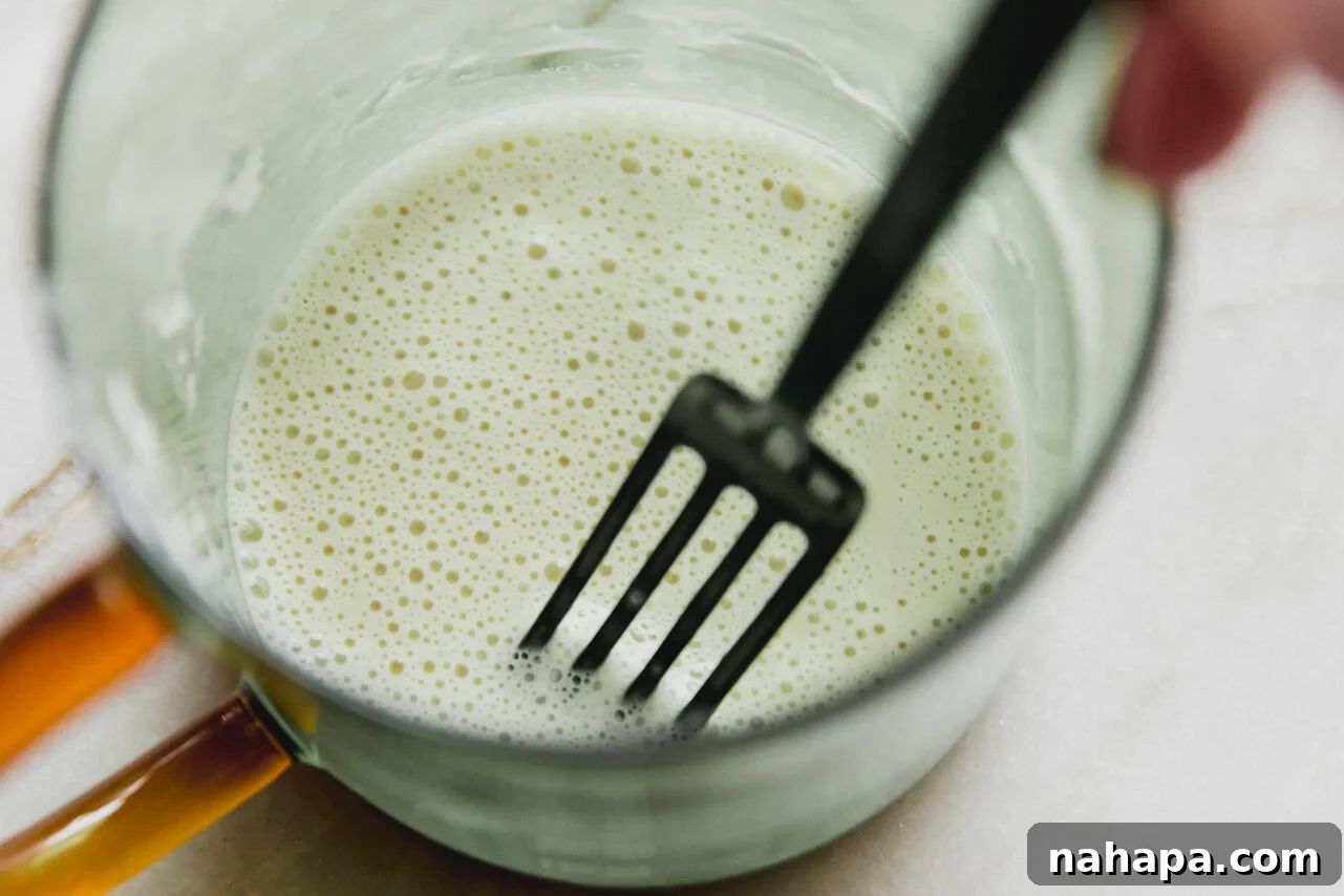 A fork mixing arrowroot starch and water in a small bowl to create a slurry.