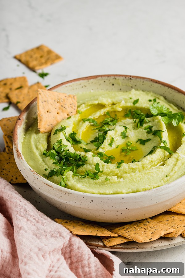 Close-up of a bowl of creamy green avocado hummus, garnished with fresh cilantro and a drizzle of olive oil, highlighting its inviting texture.