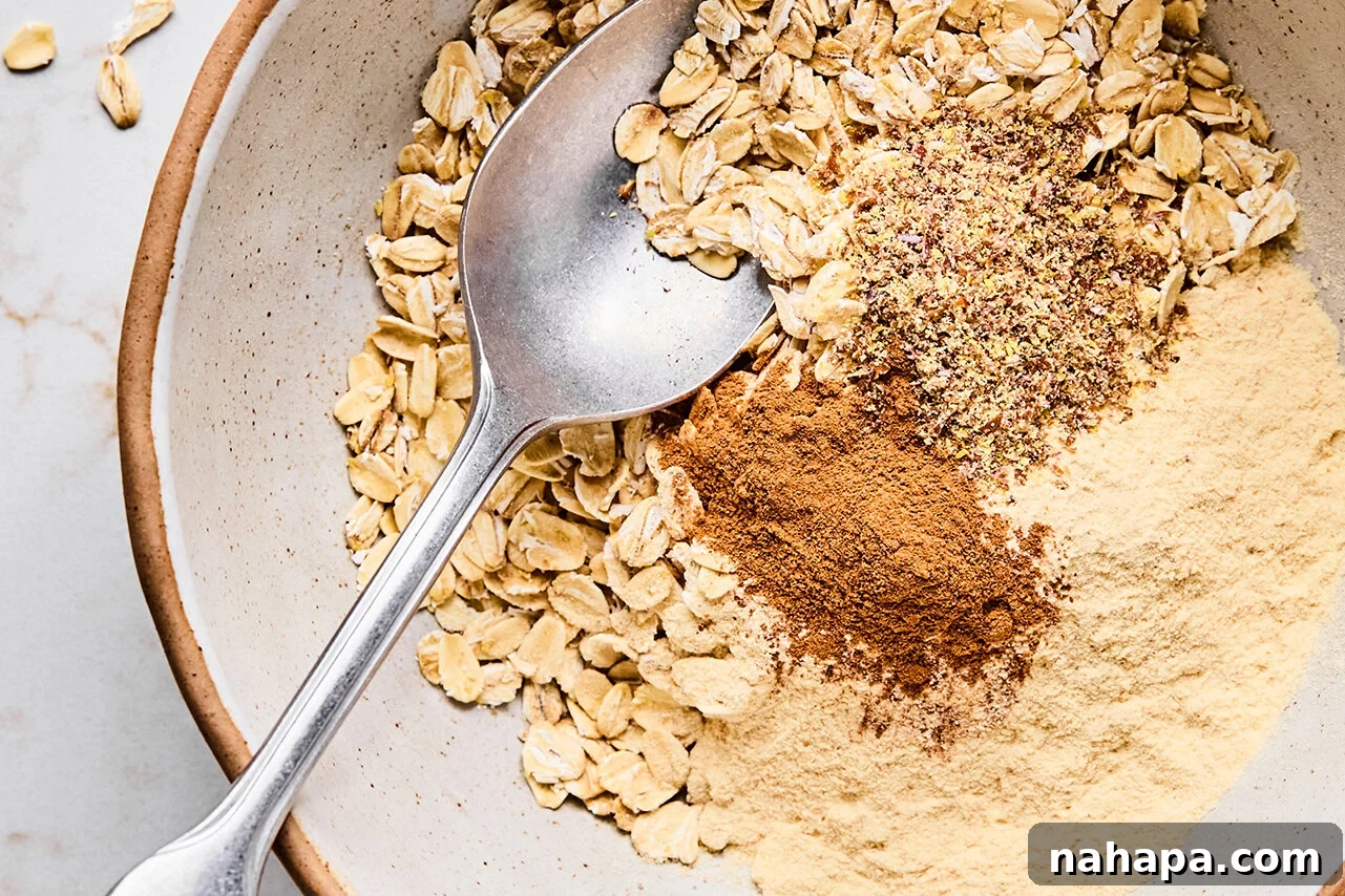 Protein-Packed Apple Crisp 4 Dry ingredients for crisp topping (oats, cinnamon, protein powder, and flax) in a bowl with a spoon before mixing.