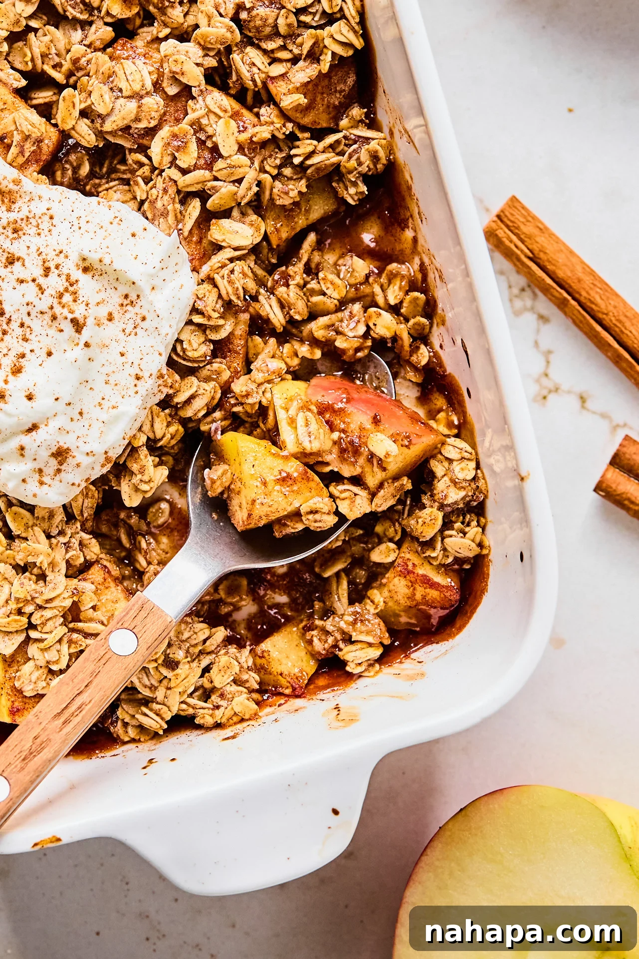 Protein-Packed Apple Crisp 10 Protein apple crisp in a baking dish with a spoon taking a small serving, garnished with fresh apple slices and a sprig of mint.
